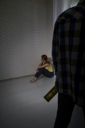 a drunk man in a worn checkered shirt with a bottle of alcohol came home to his distressed wifeの写真素材