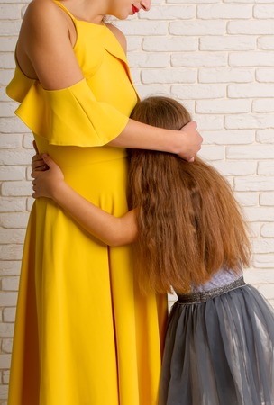 The little girl gently pressed and hugs her mom in a bright dressの写真素材