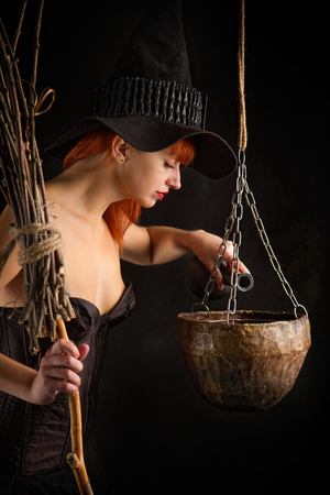 sexy girl dressed as a medieval witch with a broom in her hand conjures over a cauldronの写真素材