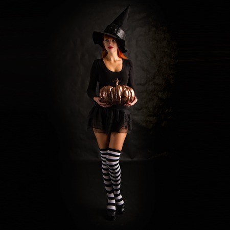 sexy girl dressed as a medieval witch stands with a pumpkin in their handsの写真素材