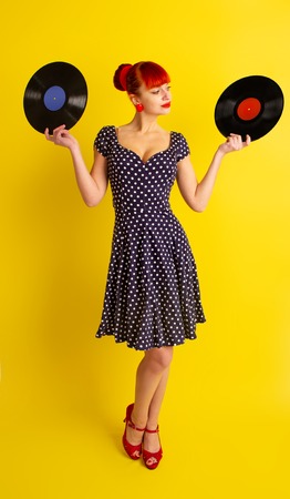 Pretty girl in retro dress in polka dot holding vinyl discs on a bright yellow backgroundの写真素材