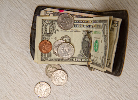 an old leather wallet of a very not rich person with a few small dollar bills and coins lying next...