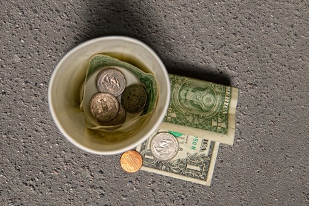 beggar's paper cup for millesti with coins and small bills on gray asphaltの写真素材