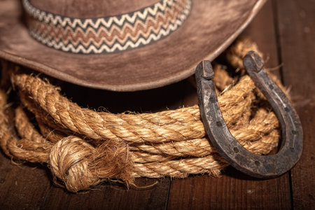 An old horseshoe lies next to a classic cowboy hat and lasso on a dark wooden background.の写真素材