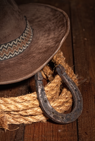 An old horseshoe lies next to a classic cowboy hat and lasso on a dark wooden background.の写真素材