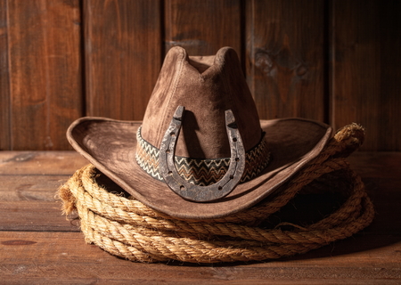 An old horseshoe lies next to a classic cowboy hat and lasso on a dark wooden background.の写真素材