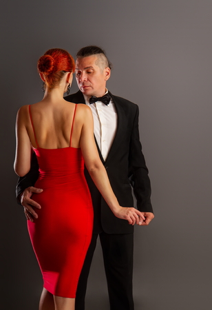 A man in a strict dark suit and a beautiful girl in a bright red dress are dancing a slow sensual dance on a dark background.の写真素材