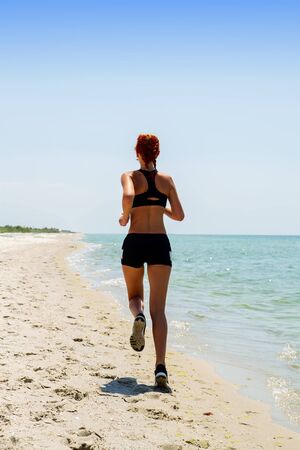 young girl in sportswear jogging on a deserted sea coastの写真素材