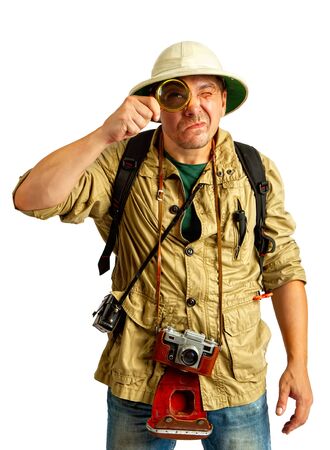 An adult tourist in a cork helmet and protective clothes wearing a camera around his neck is skeptical looking at something in a magnifying glassの写真素材