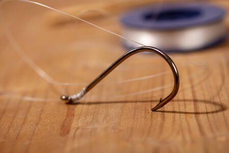 Large classic fishing hook with a thin fishing line tied to it in a reel on a wooden backgroundの写真素材