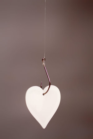 A large classic fishing hook on which a stylized heart hangs a symbol of loveの写真素材