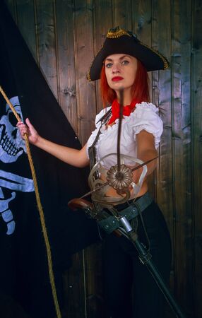 Young attractive armed girl pirate captain looks into the distance on the background of the flag Jolly Rogerの写真素材