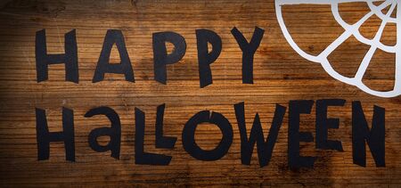 Happy Halloween handwritten scissors from black paper on a wooden surface next to a web of white paperの写真素材