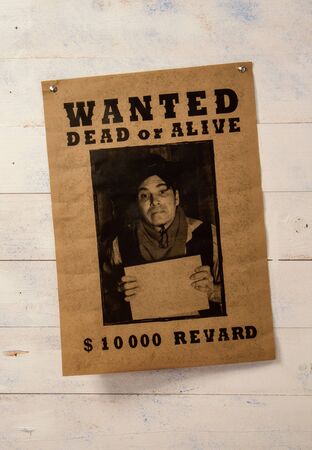 old paper announcement of criminal search and reward on yellowed paper pinned to a rough wooden wallの写真素材