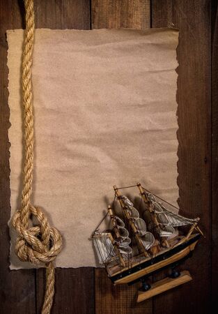 old sheet of parchment or paper lying on wooden boards and a coarse rope pulled into a nautical knot forming a frameの写真素材