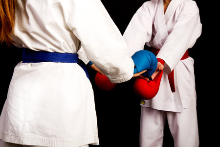 Two little karate women in white kimonos, one in red and the other in blue competition equipment...