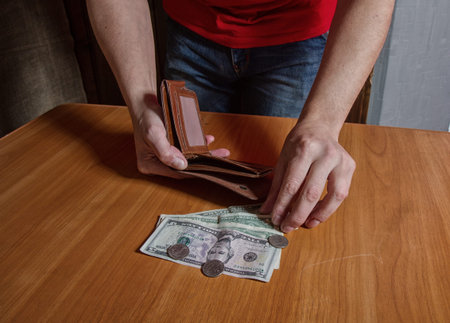 sad man in a rather poor interior considers the balance of cash in front of him...
