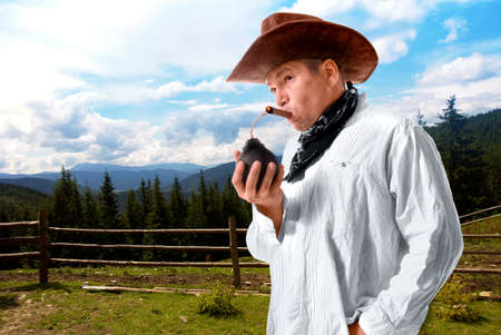 Adult male cowboy with wide-brimmed hat sets fire to a lighted cigar bomb on a ranchの写真素材