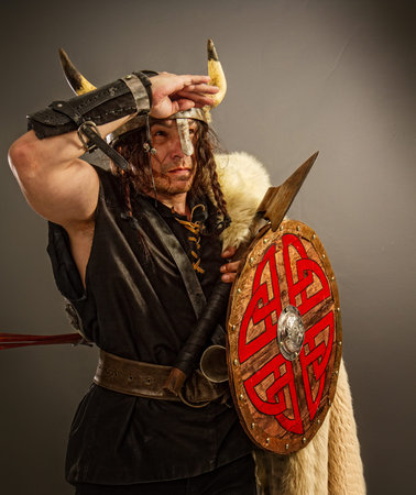 A brave viking warrior man in a horned helmet with an ax and a shield on a dark background