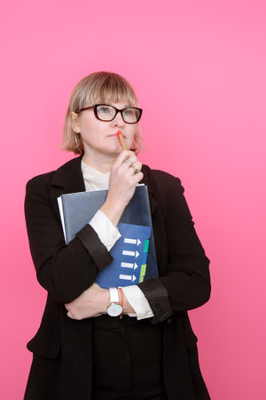 business woman in a formal suit and glasses is thinking on a pink backgroundの写真素材