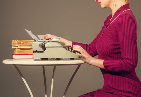 A slender elegant girl in a dress is typing something on an old typewriterの写真素材