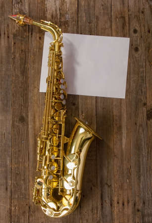 elegant classic musical instrument bronze saxophone on old wooden background with sheet of blank paper with place for textの写真素材