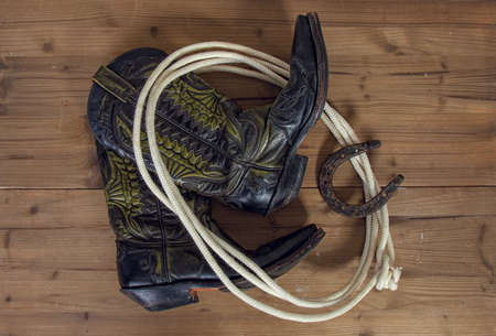Shabby old ornate classic cowboy boots horseshoe and lasso on wooden backgroundの写真素材