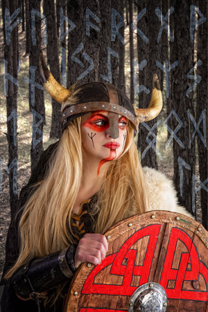 A beautiful blonde viking girl in a horned helmet is pensively standing with a shieldの写真素材