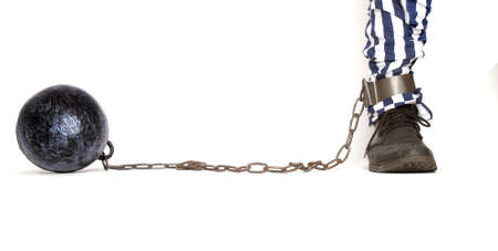 a leg of a prisoner in striped pants and a rough boot chained with an iron ball with shackles in frontの写真素材