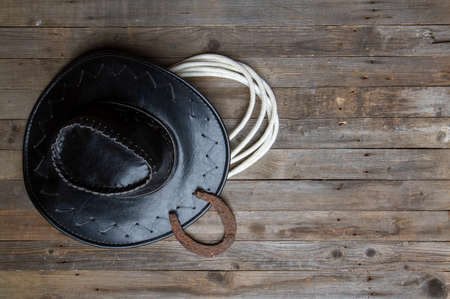 leather classic cowboy hat with lasso and horseshoe on rough wooden tableの写真素材