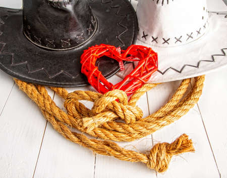 Conceptual image of a rural wedding of cowboys. White bride hat and dark groom hat and red heart symbol of loveの写真素材