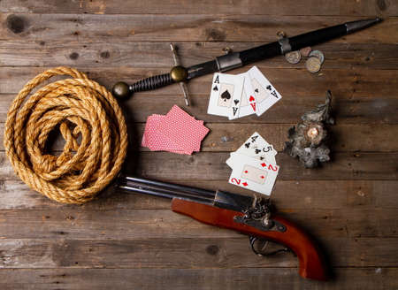 Playing cards in a pirate style, among the weapons spread out on a rough wooden table by the light of a candleの写真素材