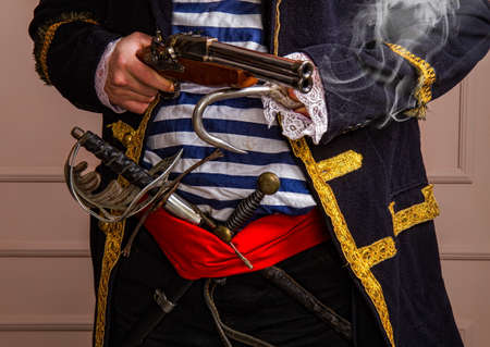 Brave armed pirate captain in a frock coat and vest with a sword and dagger and a smoking gun close-upの写真素材