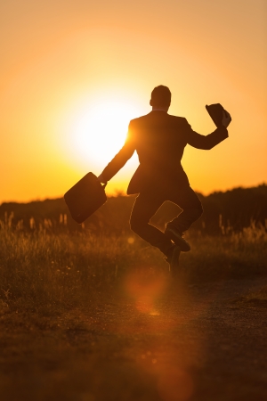 A lucky young man with bag and hat jumps in the sundownの写真素材