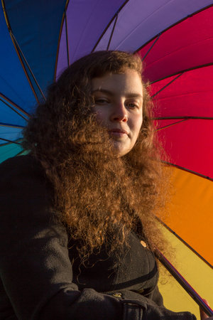 A young pretty woman sits with a coloured umbrella in the winter sun