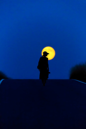A woman walks a street at full moonの写真素材