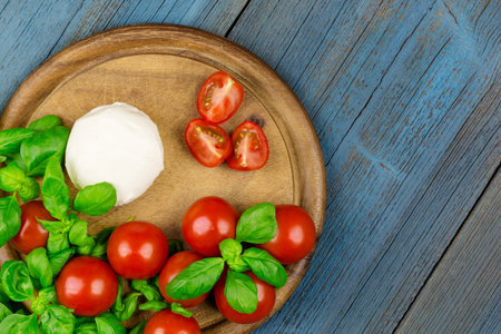 A board with tomato, mozzarella and basil on blue woodの写真素材