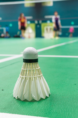 White badminton shuttlecock on a green floor with blurred players in badminton court.の写真素材