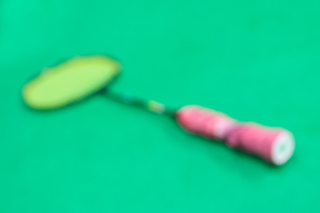 Blurred black badminton racket with red grip and yellow net on the green court.の写真素材