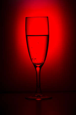 A glass of champagne on a dark background with a red light.の写真素材