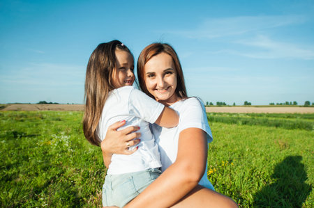 The mother is holding a baby girl.Sunday rest, flower field. Loving mother plays with daughter, hugs and kissesの写真素材
