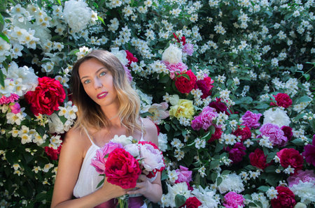 Beautiful happy and sexy young woman, a bride in a white dress enjoys the smell of flowers In a blooming summer garden.の写真素材