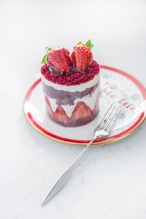 Fresh cake with strawberries on a red plate with a cup of cappuccino. Food and Christmas mood on a whiteの写真素材