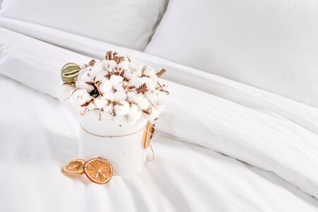 Original and beautiful cotton flowers bouquet in a white bowle on the white bed with duvet and pillows. Cozy bedroom.の写真素材