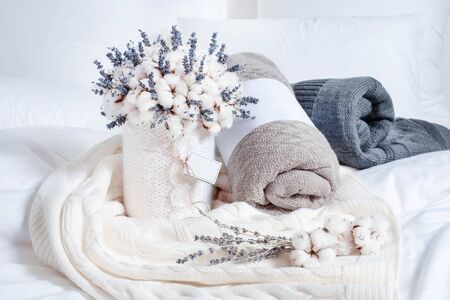 Creative composition with rolled blankets, cotton and lavender flowers. Brown, white and gray plaids on the bed. Cozy set of bedding and flowers.の写真素材