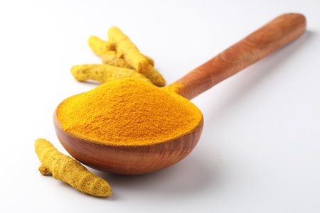 Turmeric powder in wooden spoon with turmeric roots on white background.の写真素材