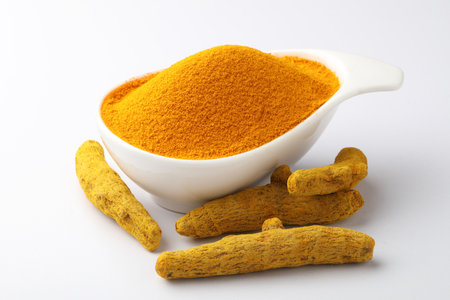 Turmeric powder in a bowl with turmeric roots on white backgroundの写真素材