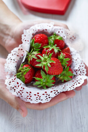 Man's hand with fresh strawberries for Valentine's Day in a heart shaped boxの写真素材