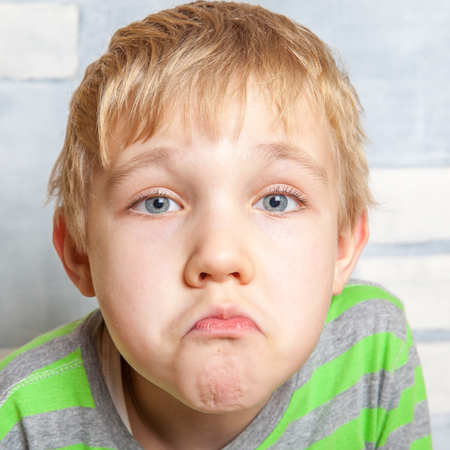 Portrait of adorable sad funny child on wall backgroundの写真素材