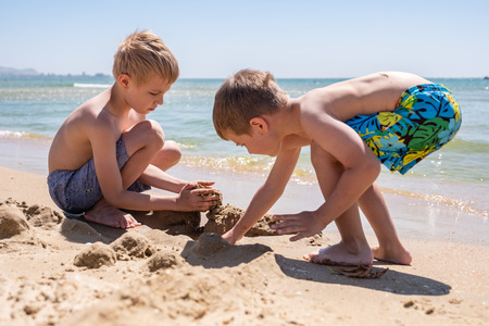 Happy child playing with sand at the beach in summerの写真素材